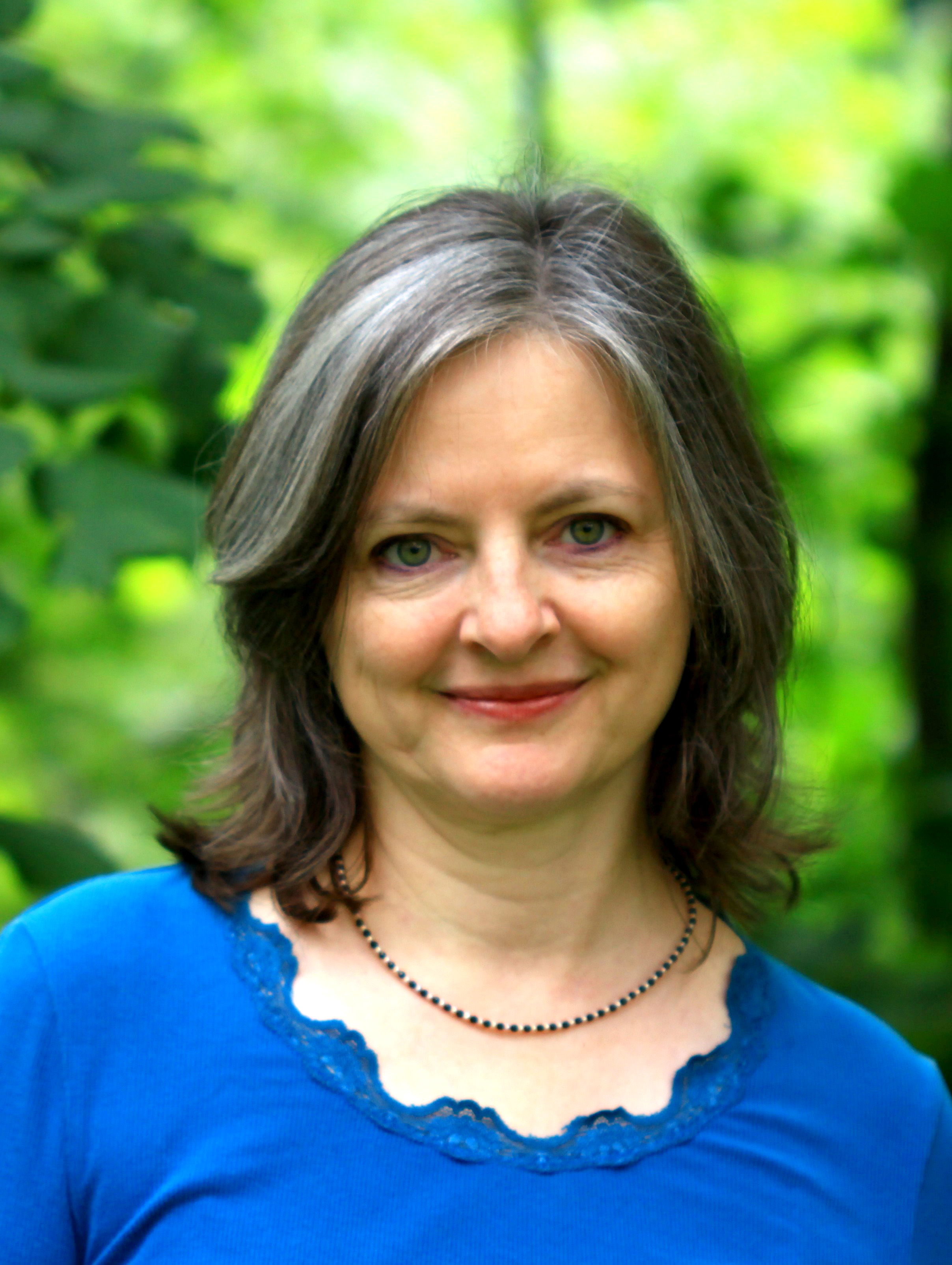 Antje Lohrer, Ordnungsberaterin, freundlich lächelnd im grünen Wald, in einem blauen Oberteil.